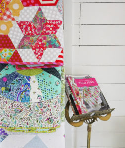 Three quilts are displayed in Tula Pink's office, alongside her book, Quilts from the House of Tula Pink.