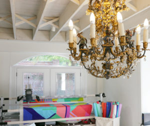 An antique chandelier that features monkeys overlooks Tula Pink's long-arm quilting machine.