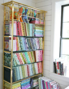 A golden shelf filled with Tula Pink's library of quilting fabric.