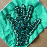 A green and blue beaded handprint, a part of a larger project that Nedra is working on.