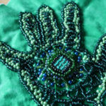 A green and blue heavily beaded handprint.