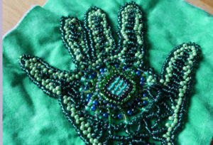A green and blue heavily beaded handprint.