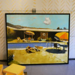 A Seth Smith painting of a retro pool scene leans agains a garage door carefully decorated with gold dashes.