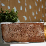A brick stamped Lawrence, Kansas sits on a bookcase in Seth Smith's studio.
