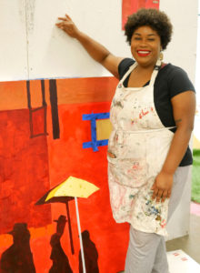 Glyneisha stands next to her current work in progress, a bright red collage based on a scene from the movie Do The Right Thing.