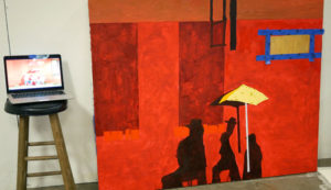 A large scale painting leans against the wall. Glyneisha is working on it with her source material close by on a laptop.
